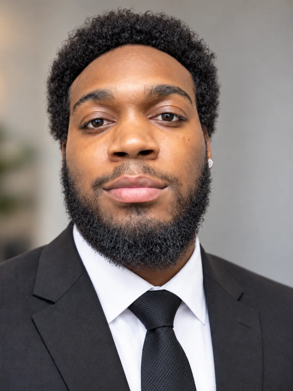 Portrait of Khaylub Thompson-Calvin wearing a dark suit and tie, looking at the camera.