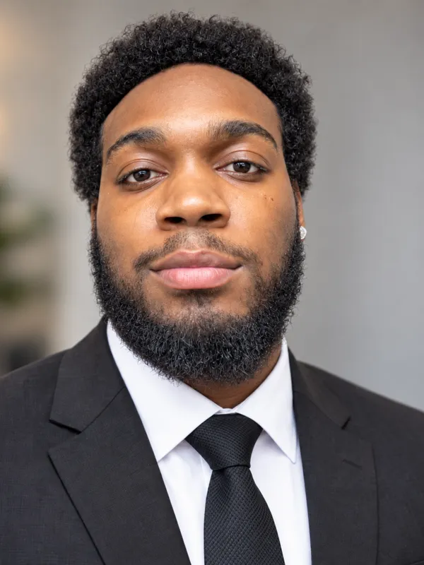 Portrait of Khaylub Thompson-Calvin wearing a dark suit and tie, looking at the camera.